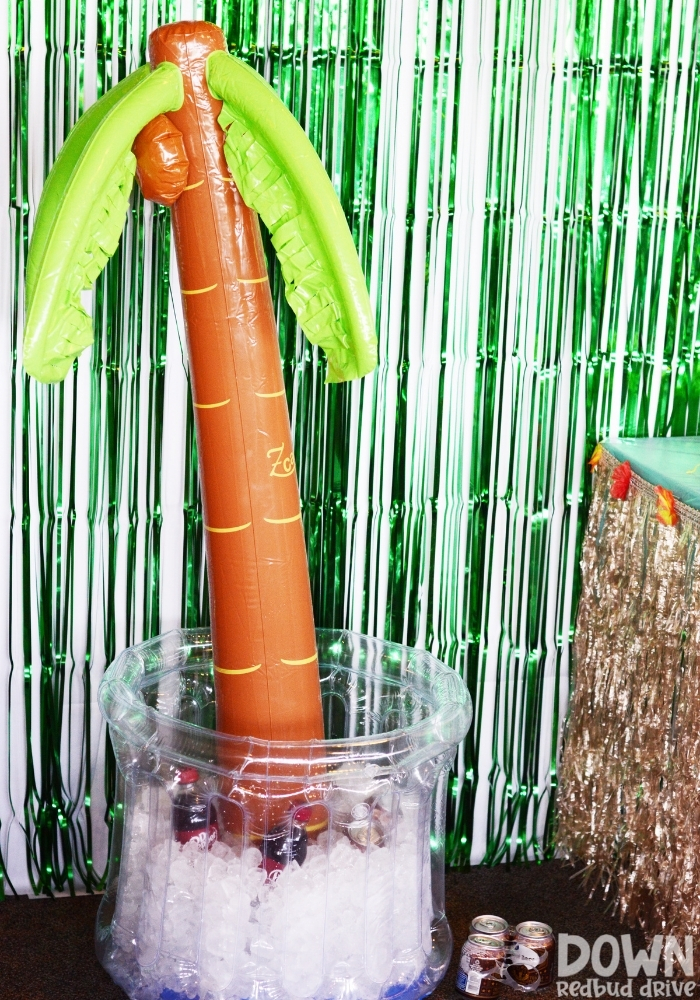 A blow-up palm tree cooler with ice, soda and water bottles in it.