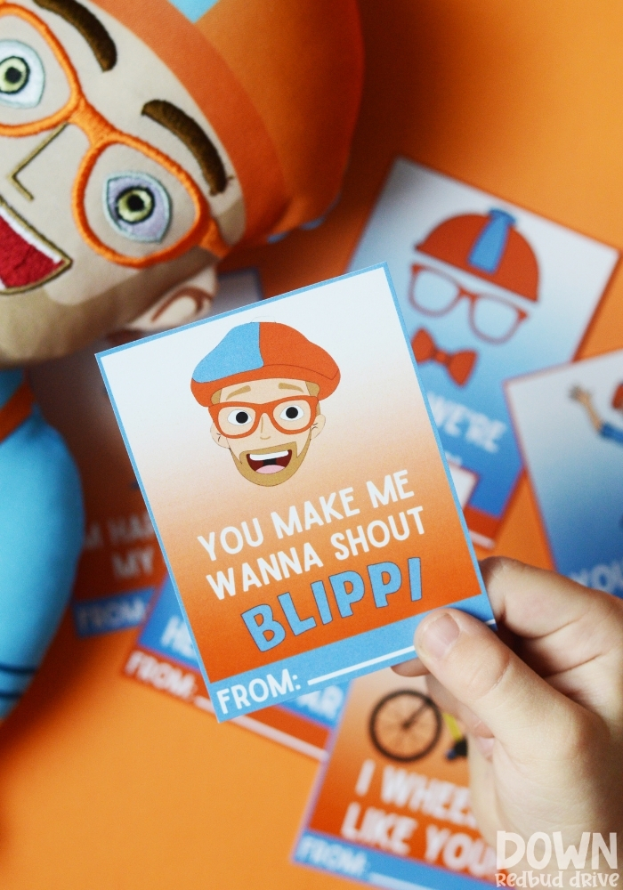 A tall image of a child holding a valentine that says, "You make me wanna shout Blippi" on it with more valentines in the background.