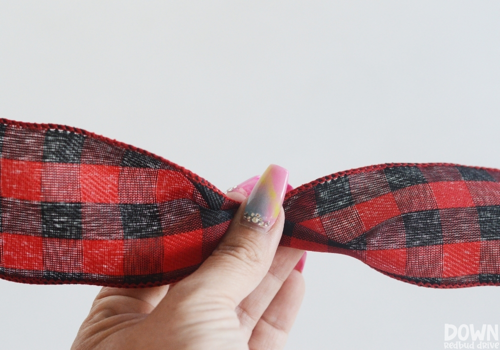 A hand pinching red and black buffalo check ribbon together to make a bow shape.