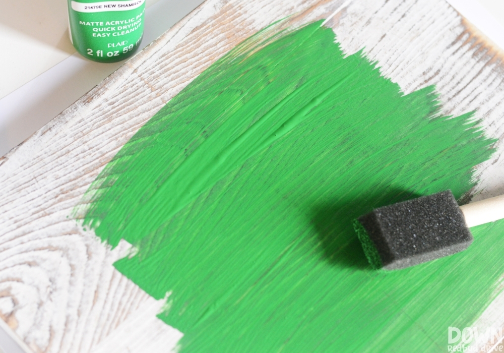 Overhead view of a wooden sign being painted green.