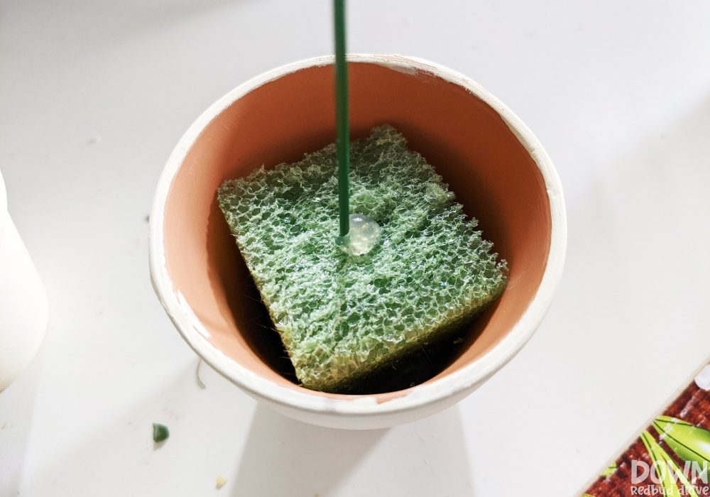 Overhead view of a decorative Easter pick being glued into floral foam for the DIY Easter Egg Topiary.