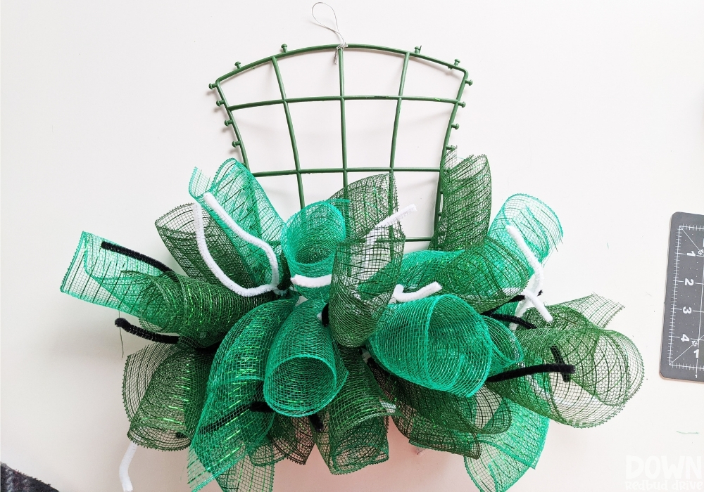 A hat wreath base with green rolled mesh attached with pipe cleaners.