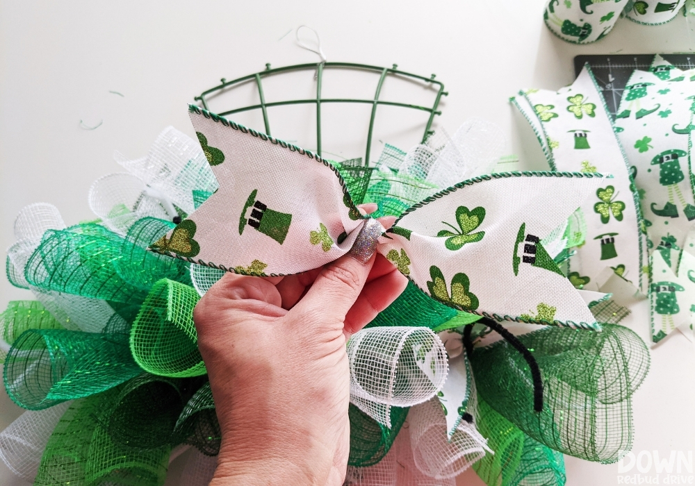 Showing how to pinch and hold ribbon to attach it to a mesh wreath.