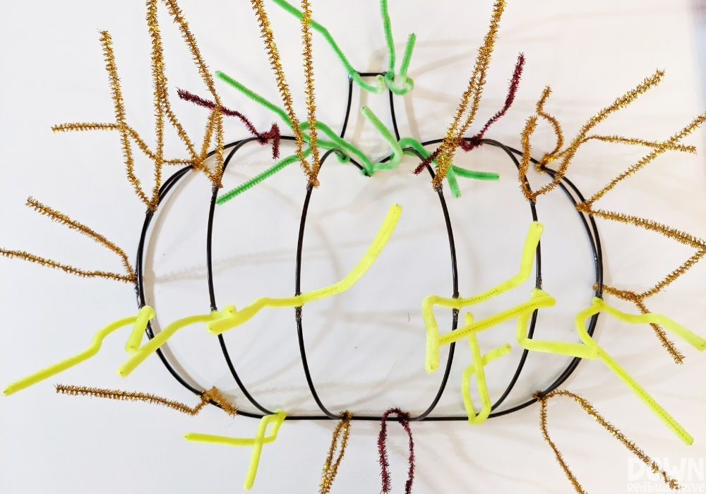 Gold, green and yellow pipe cleaners attached to a pumpkin wreath shape.