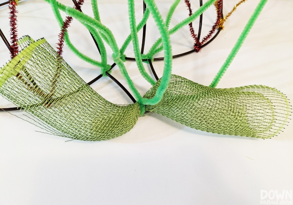 Green deco mesh attached to a pumpkin wreath form with green pipe cleaners.