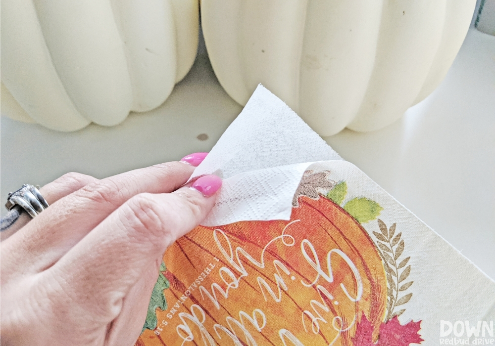 Picture of hands separating the layers of a fall pumpkin napkin.