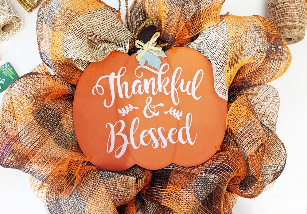 A "Thankful & Blessed" pumpkin sign attached to a fall deco mesh wreath.