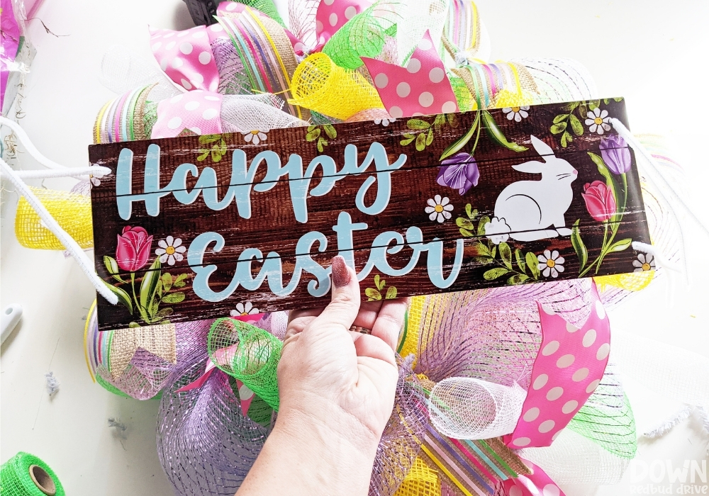 Close up of the "Happy Easter" sign with pipe cleaners threaded through holes on all four corners for attaching it to the DIY Easter mesh wreath.