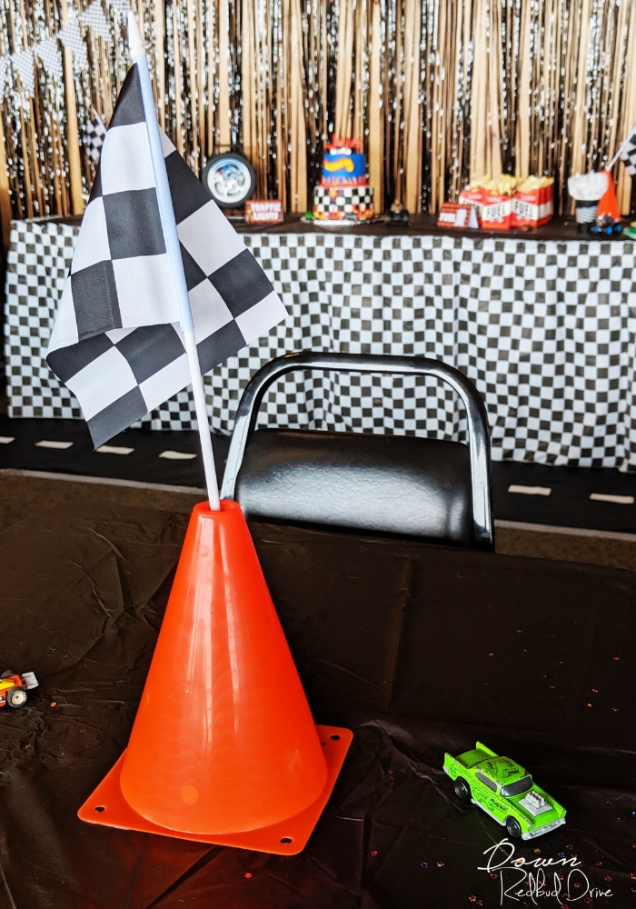 an orange tragffic cone with a black and white checkered flag stuck in the top of it sitting on a black table next to a green hot wheels car