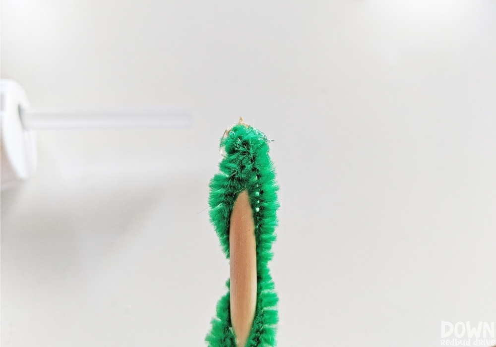 Closeup of a green pipe cleaner being wrapped around a dowel rod.