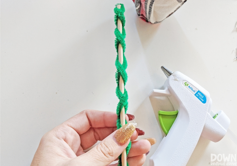 Closeup of green pipe cleaners being wrapped around a dowel rod.