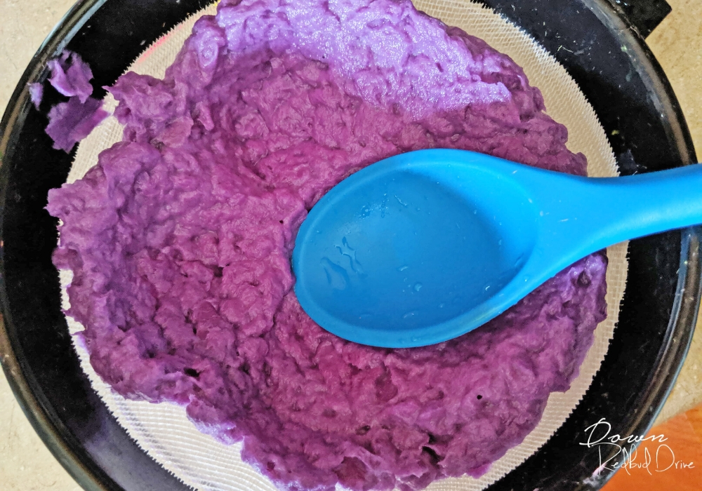 a blue spoon pressing wet paper through a mesh strainer