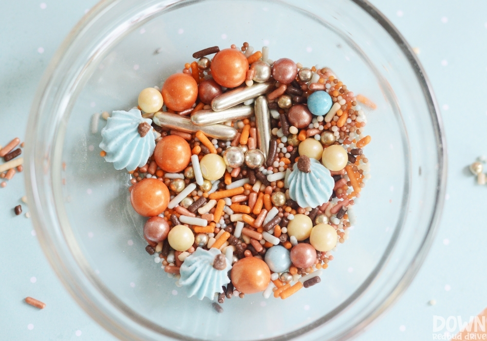 Close up of fall themed sprinkles in a clear glass bowl.