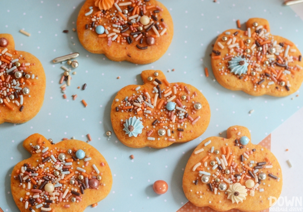 Overhead view of fall sprinkles added to pumpkin shaped cookies.