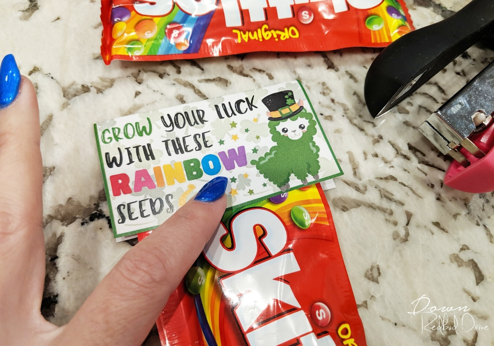 a finger holding on the Rainbow Seeds label onto a package of Skittles