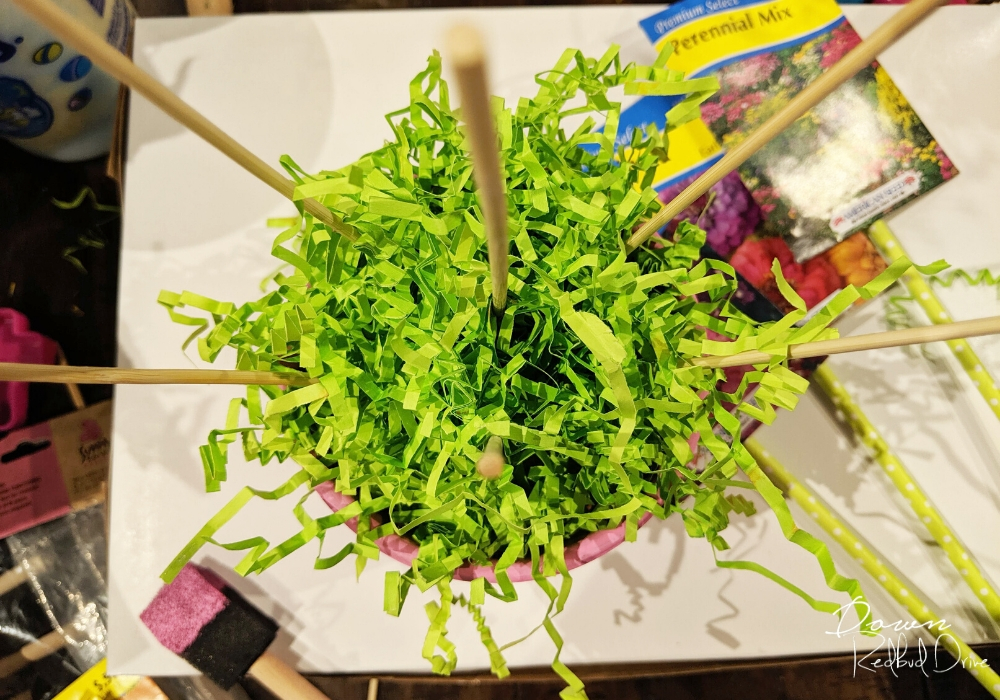 green shredded paper in a small pink flower pot with small bamboo skewers