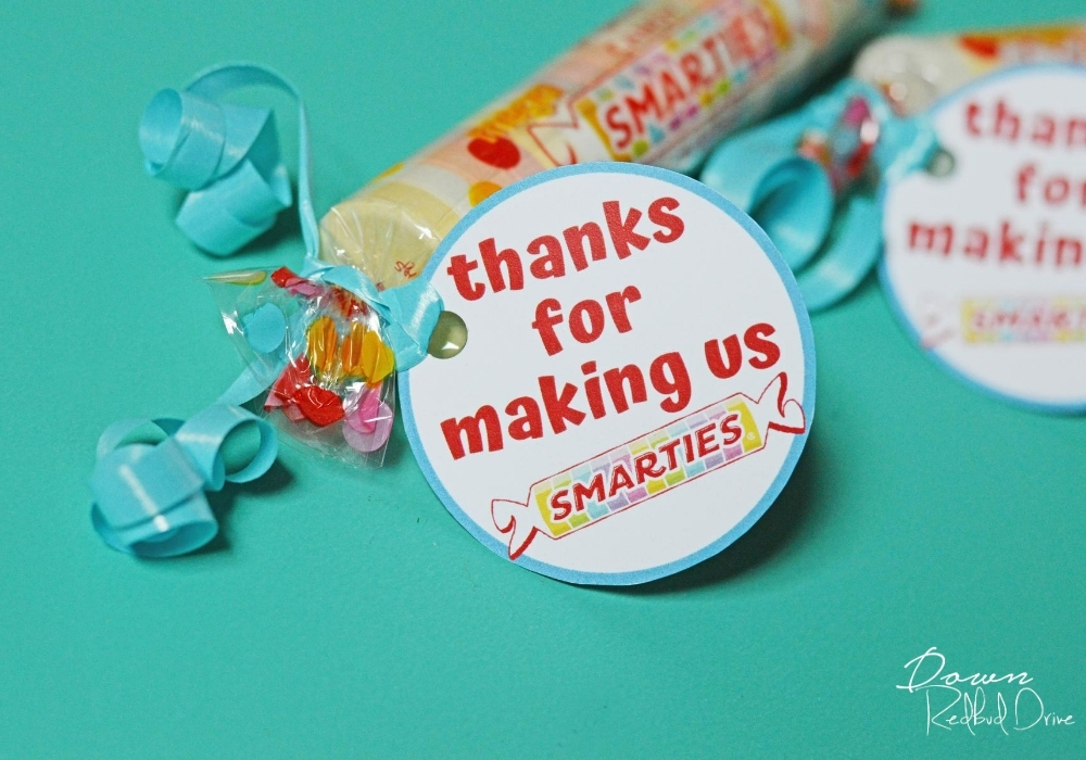 Side shot of "thanks for making us smarties" tag attached to Smarties candy with a blue ribbon.