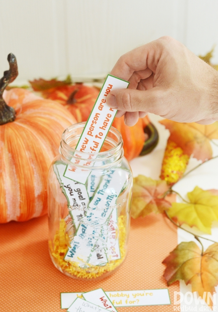 A wide closeup of a hand taking a thanksgiving gratitude game card out of a mason jar.