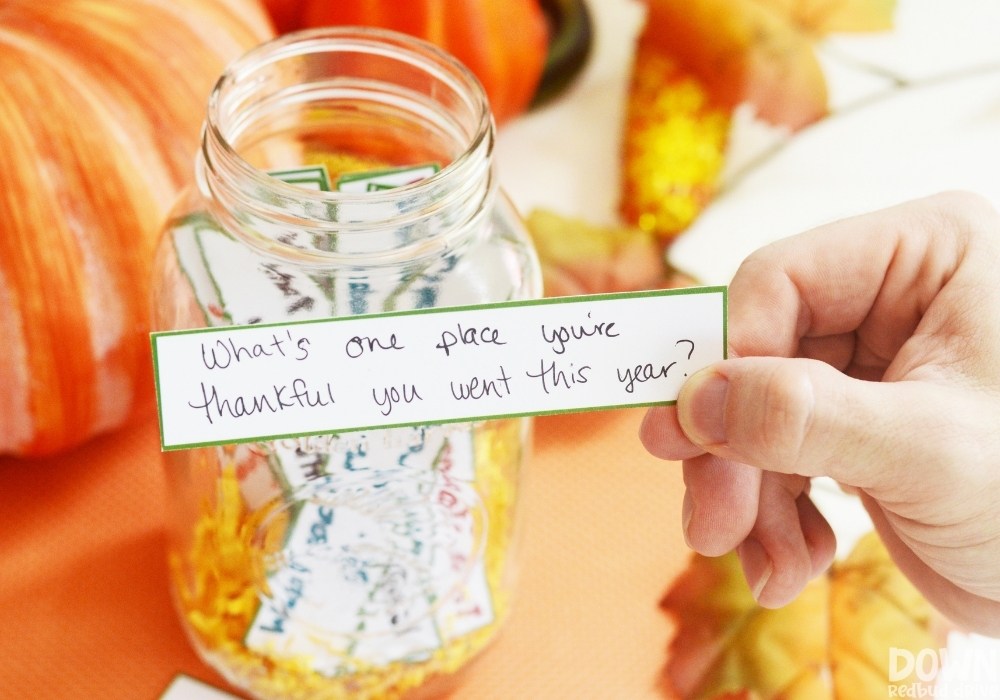 A closeup of a hand holding the question "What's one place you're thankful you went this year" from the thanksgiving conversation starters game.