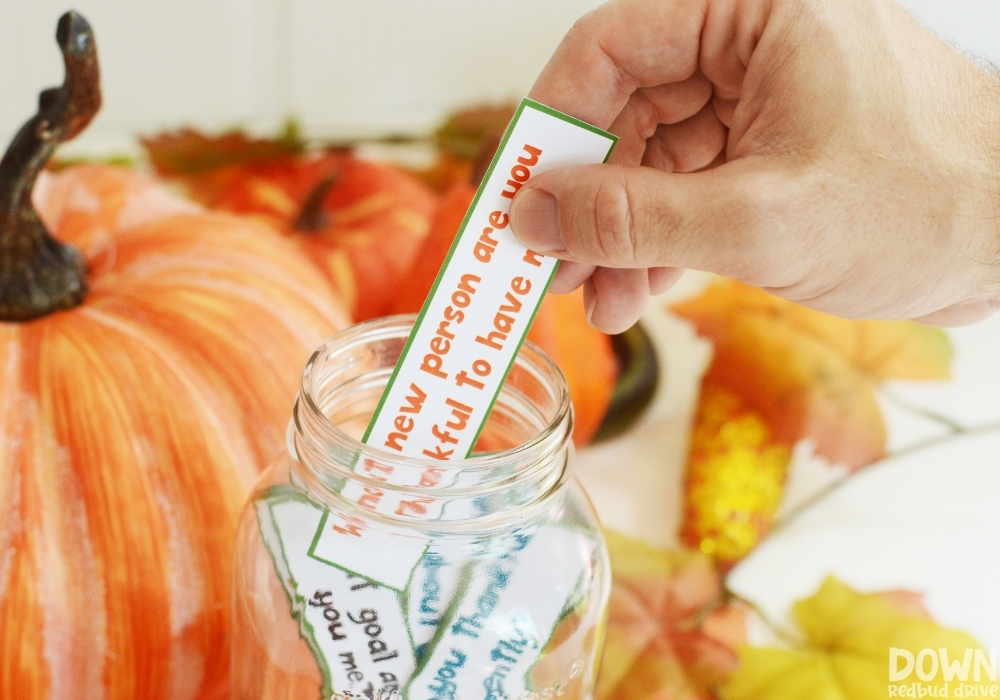 A hand taking a thanksgiving gratitude game card out of a mason jar.