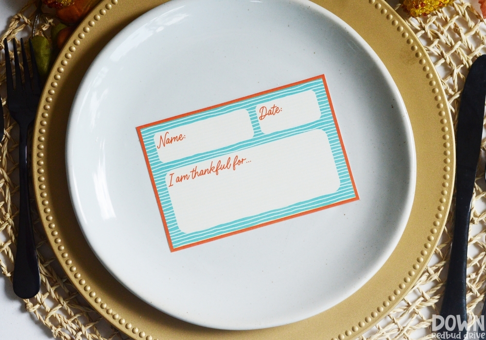 An orange and blue Thanksgiving place card on a plate.