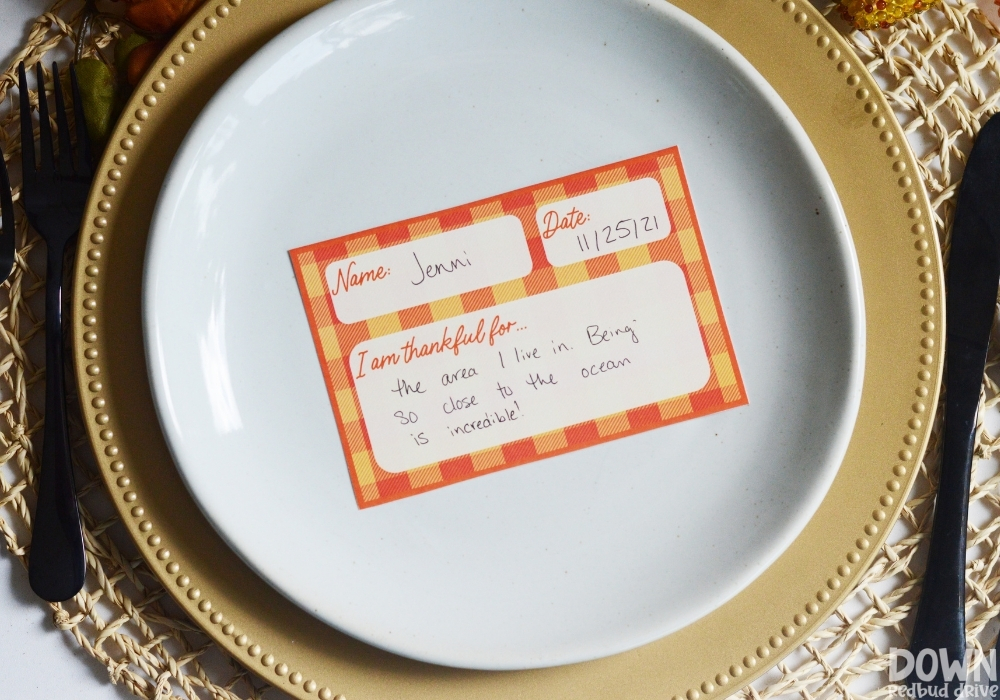 An orange and yellow plaid Thanksgiving thankful place card on a plate.