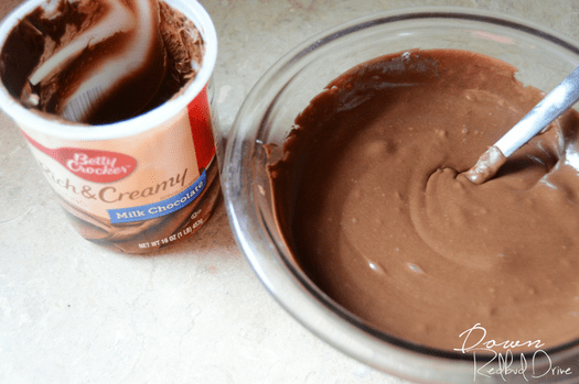 Chocolate cake frosting in a clear glass bowl.