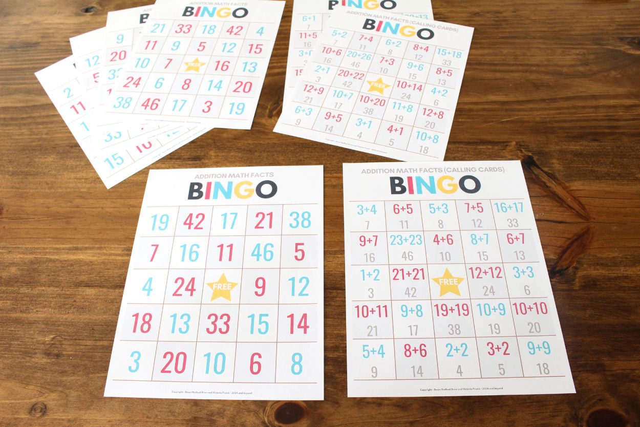 Printed sheets from the addition math facts bingo game for kids free download on a wooden tabletop