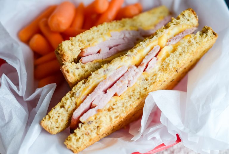 A basket of snacks including baby carrots and an air fryer ham and cheese sandwich.