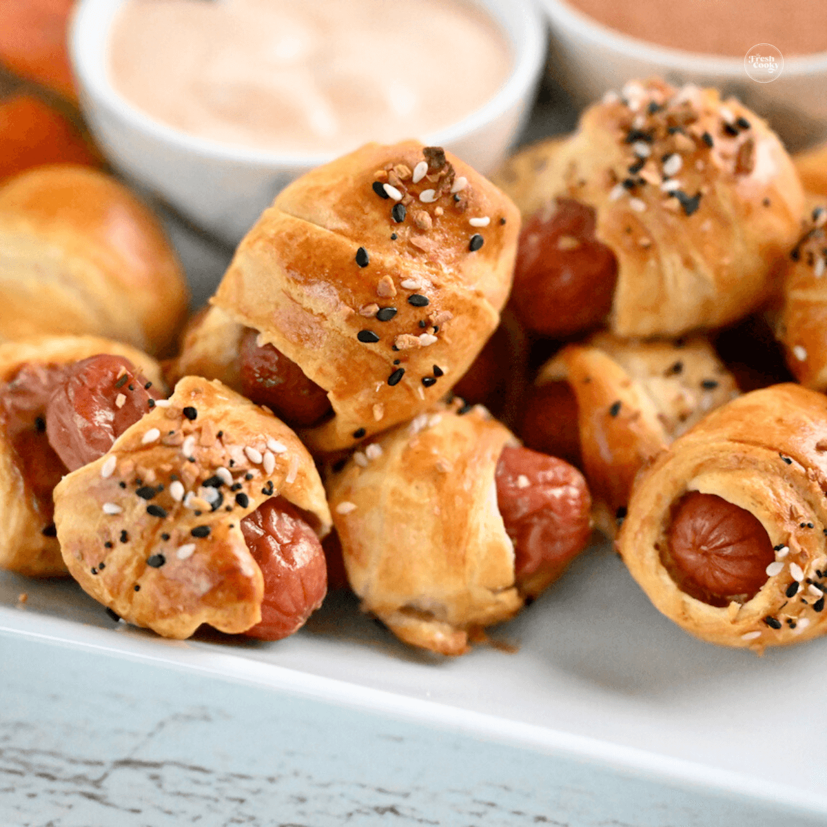 a plate of finished pigs in a blanket snacks, dipping sauce bowls in the background.