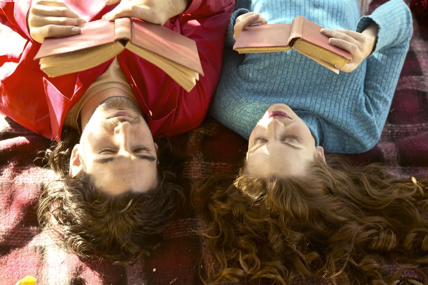 a couple laying on a plaid picnic blanket reading together.