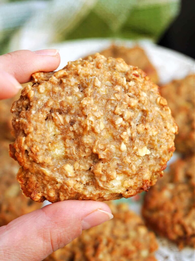 banana oatmeal cookie being held in the foreground, a plate of cookies in the background.