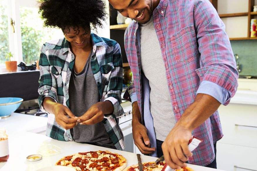 a young couple making pizza together at home, both are smiling