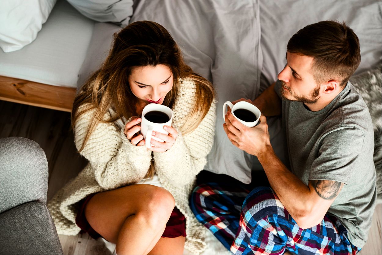 A young couple drinking coffee in front of the couch while sitting on the floor.