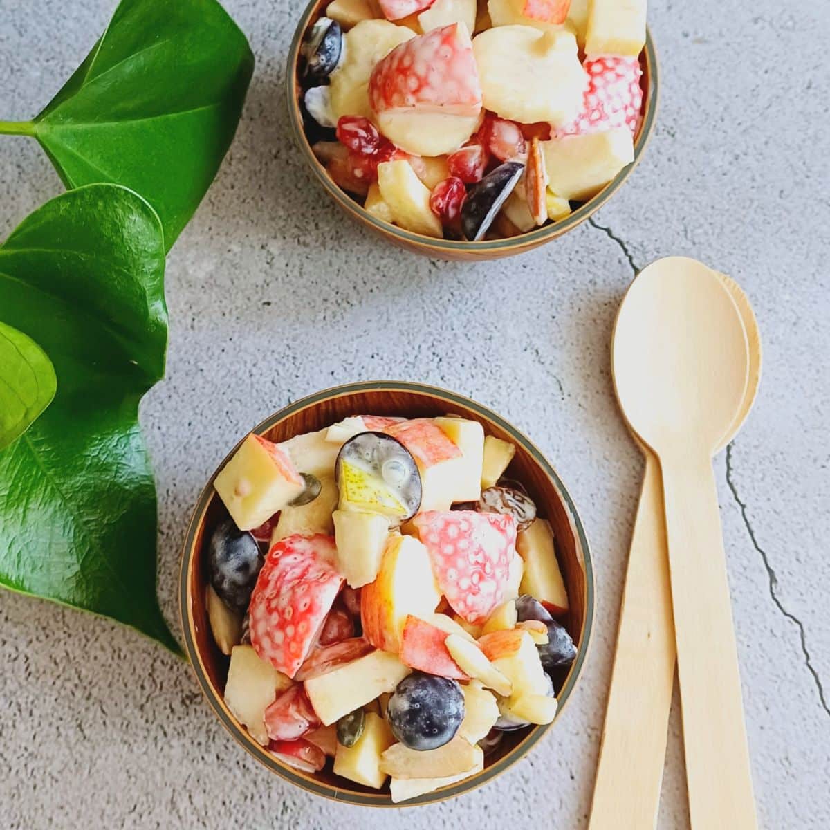 two wooden bowls of fruit salad with cream, 2 wood spoons next to the bowls.