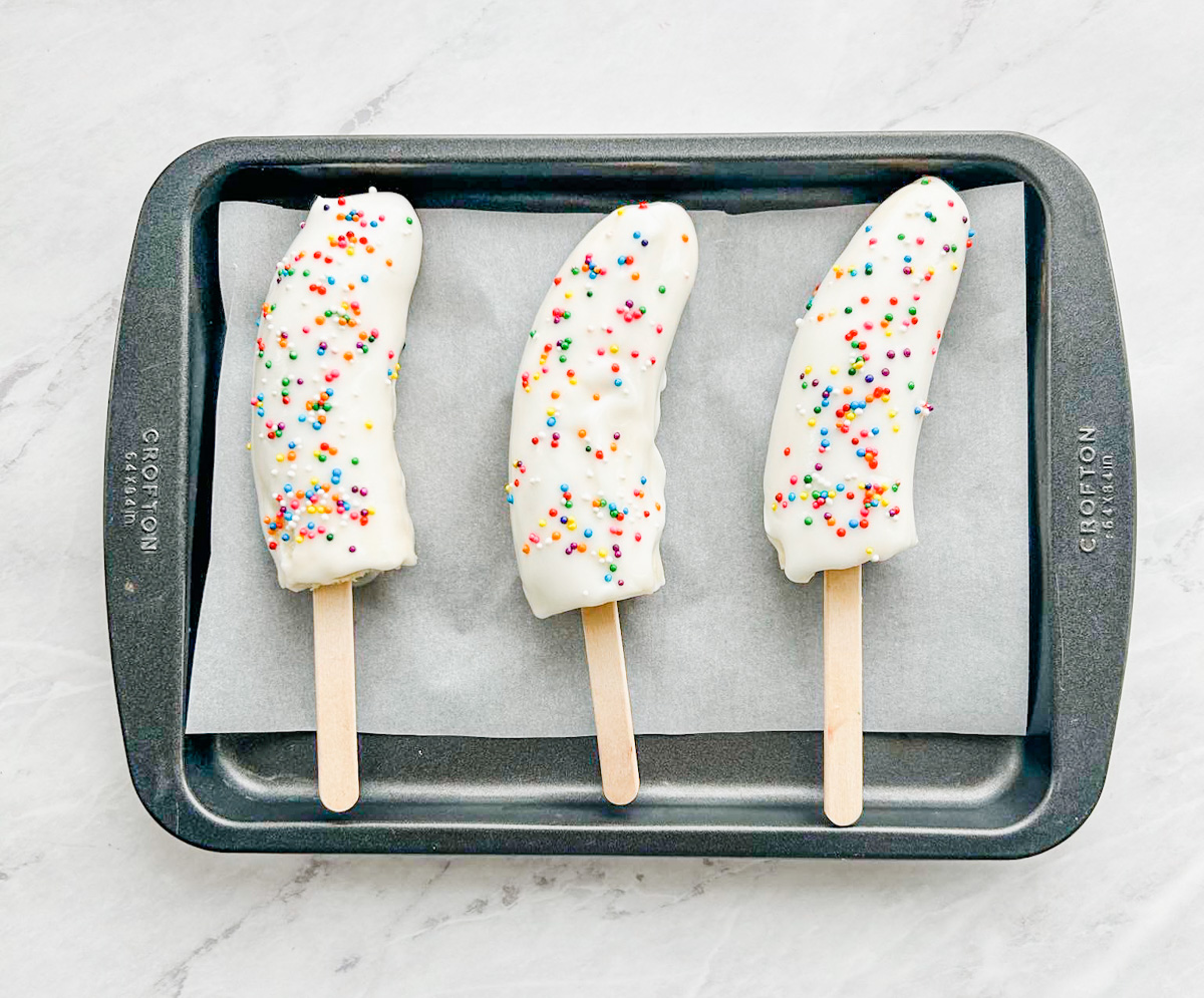 Frozen bananas covered in white chocolate and colored sprinkles.