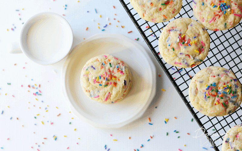 a plate of rainbow sugar cookies next to a cooling rack with more cookies on it too.