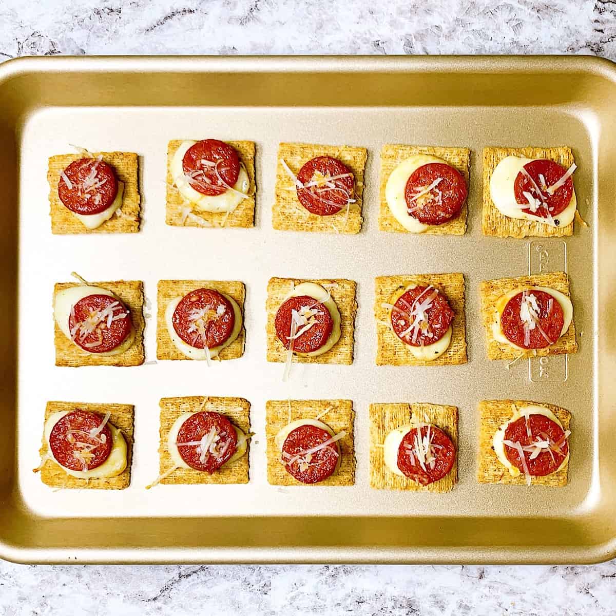 an oven tray with triscuit crackers covered in cheese and pepperoni