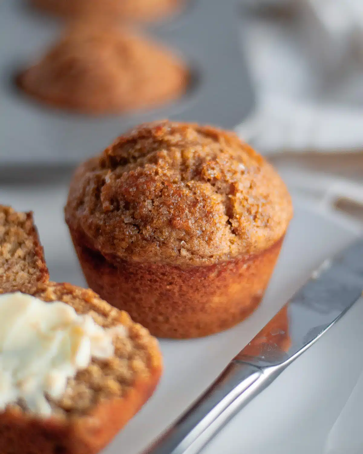 a single wheat germ muffin in the foreground with a pan of muffins in the background.