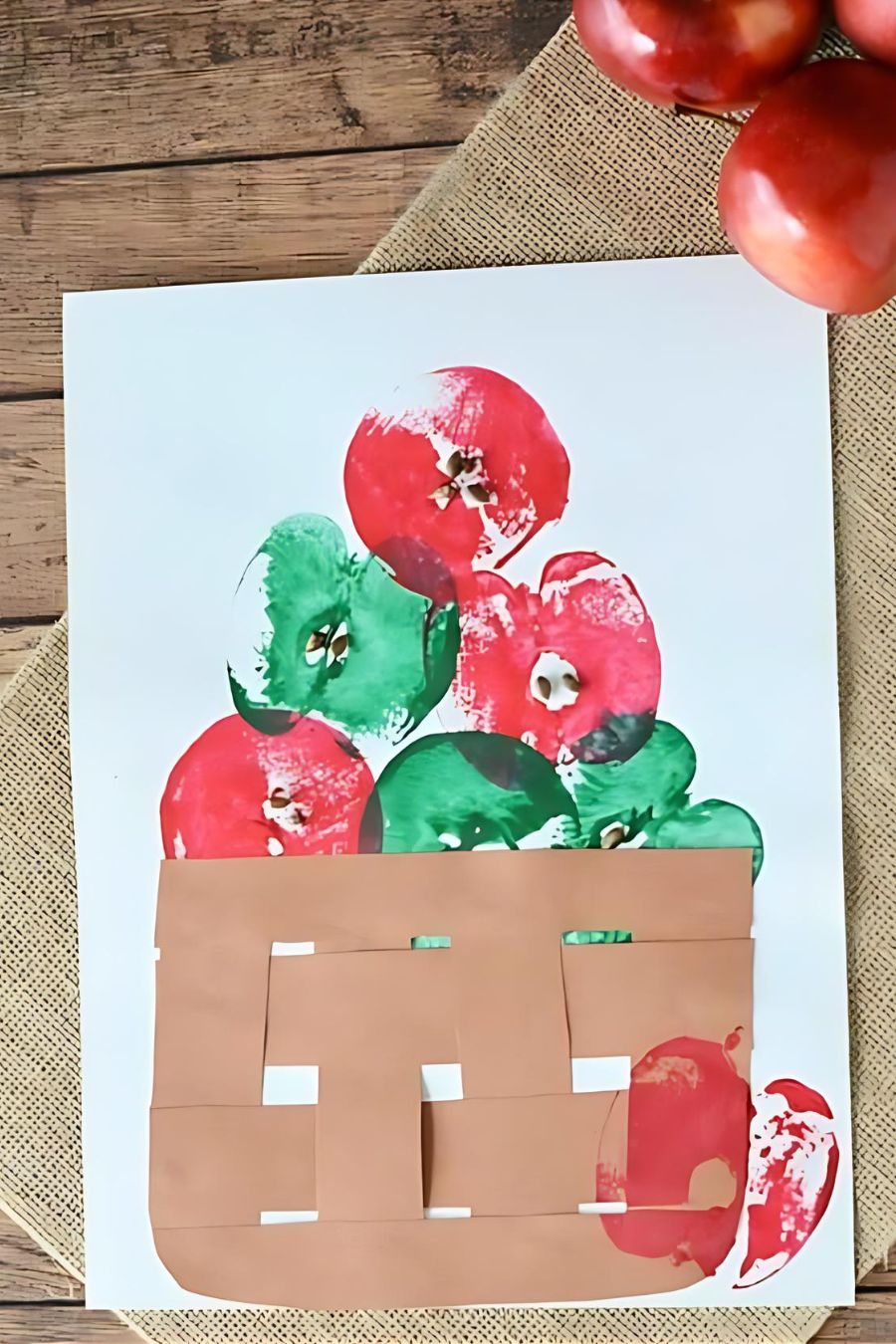 A piece of paper decorated with paint to look like a bushel of apples, real apples were used as paint stamps