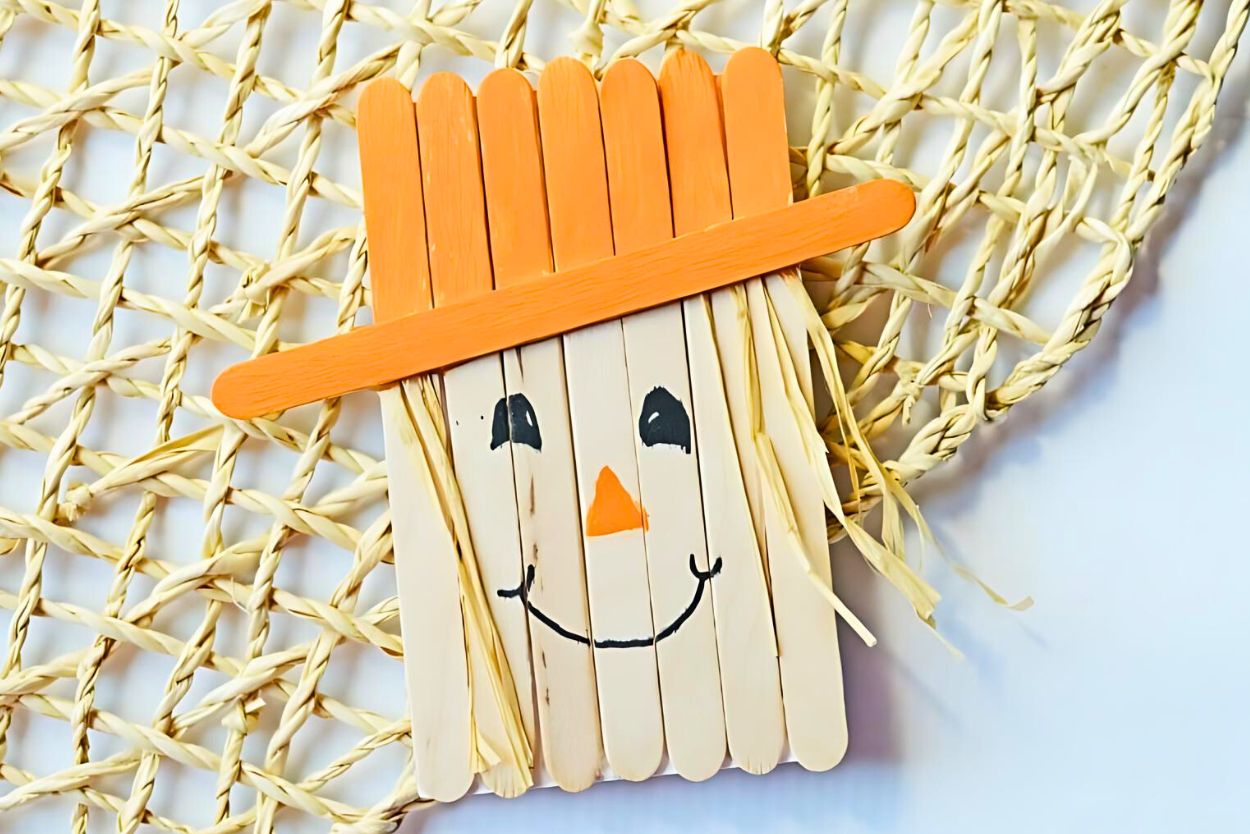 Finished popsicle stick scarecrow magnet fall craft on a woven jute background.