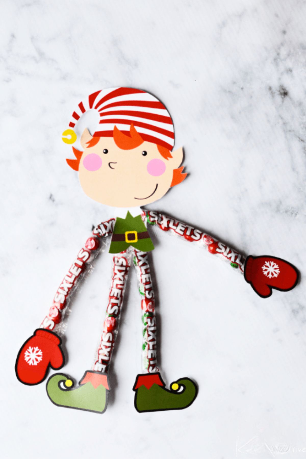 a cute paper elf with arms and legs made out of sixlets candy in the wrapper