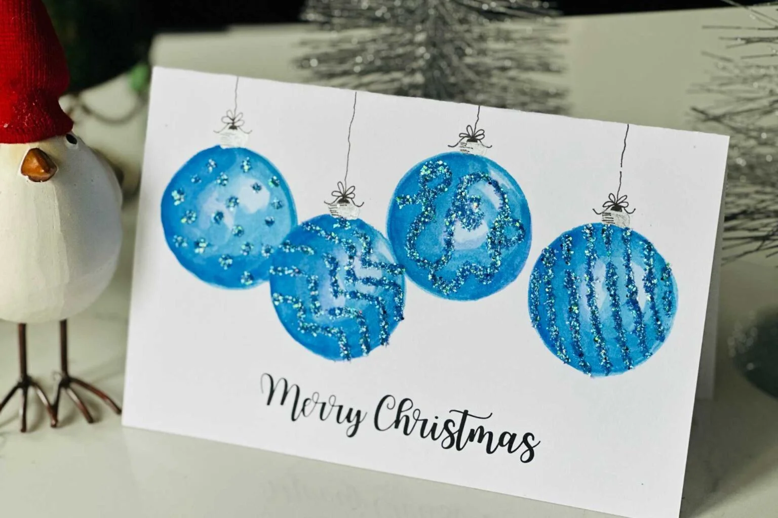 finished watercolor christmas card with 4 blue ornaments with glitter on the front