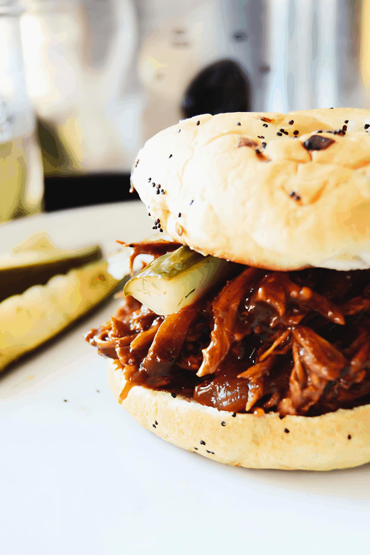 Finished crockpot bbq chicken sandwich on a white plate with several pickle spears next to it.