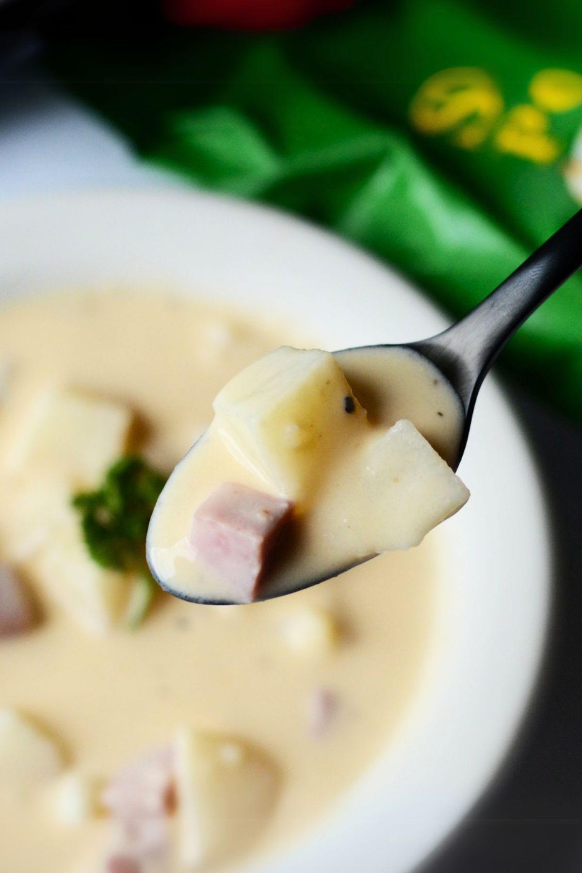 close up of a spoon of crockpot ham and potato soup with a white bowl in the background.