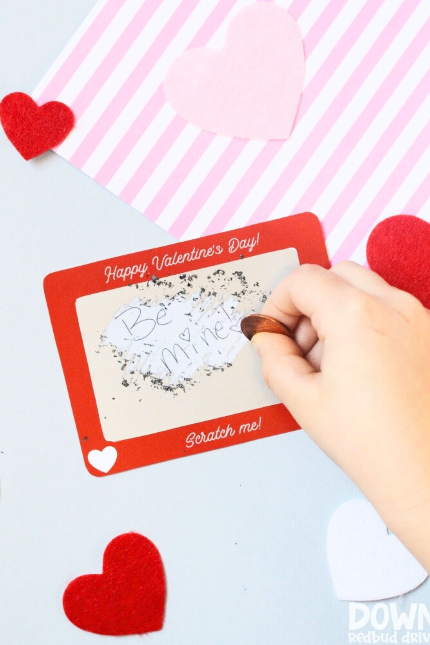 Small child scratching off the silver coating on a scratch off valentines day card that looks like an etch a sketch to reveal the words be mine.