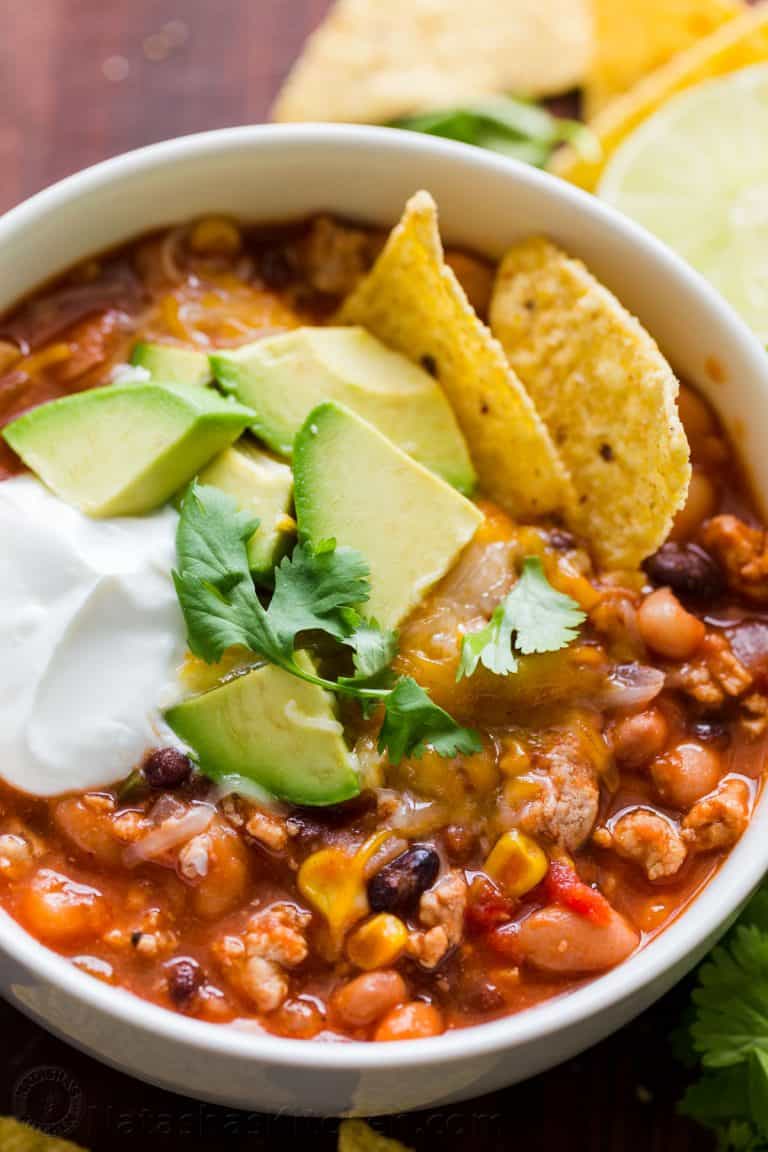 White bowl of homemade crockpot turkey chili topped with sour cream and avocados