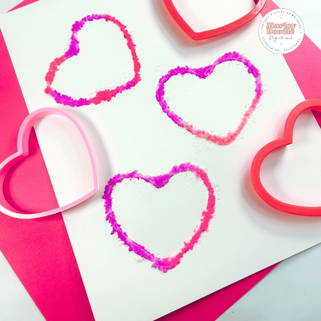 Heart shaped cookie cutters used as stamps to create a heart shaped salt painting.