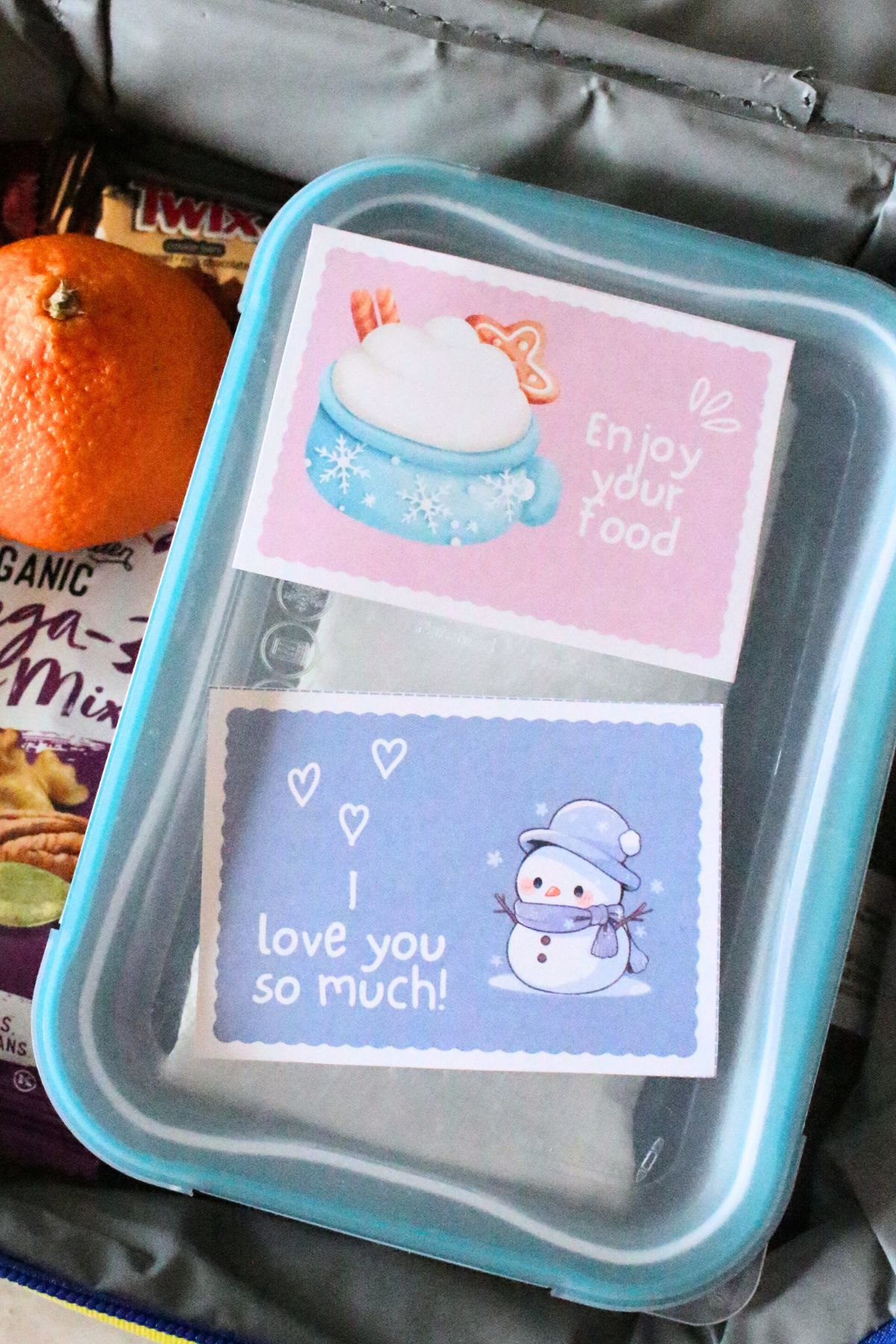 close up of a printable winter lunch box note with the words I love you so much and a cute snowman inside a packed kids school lunchbox.