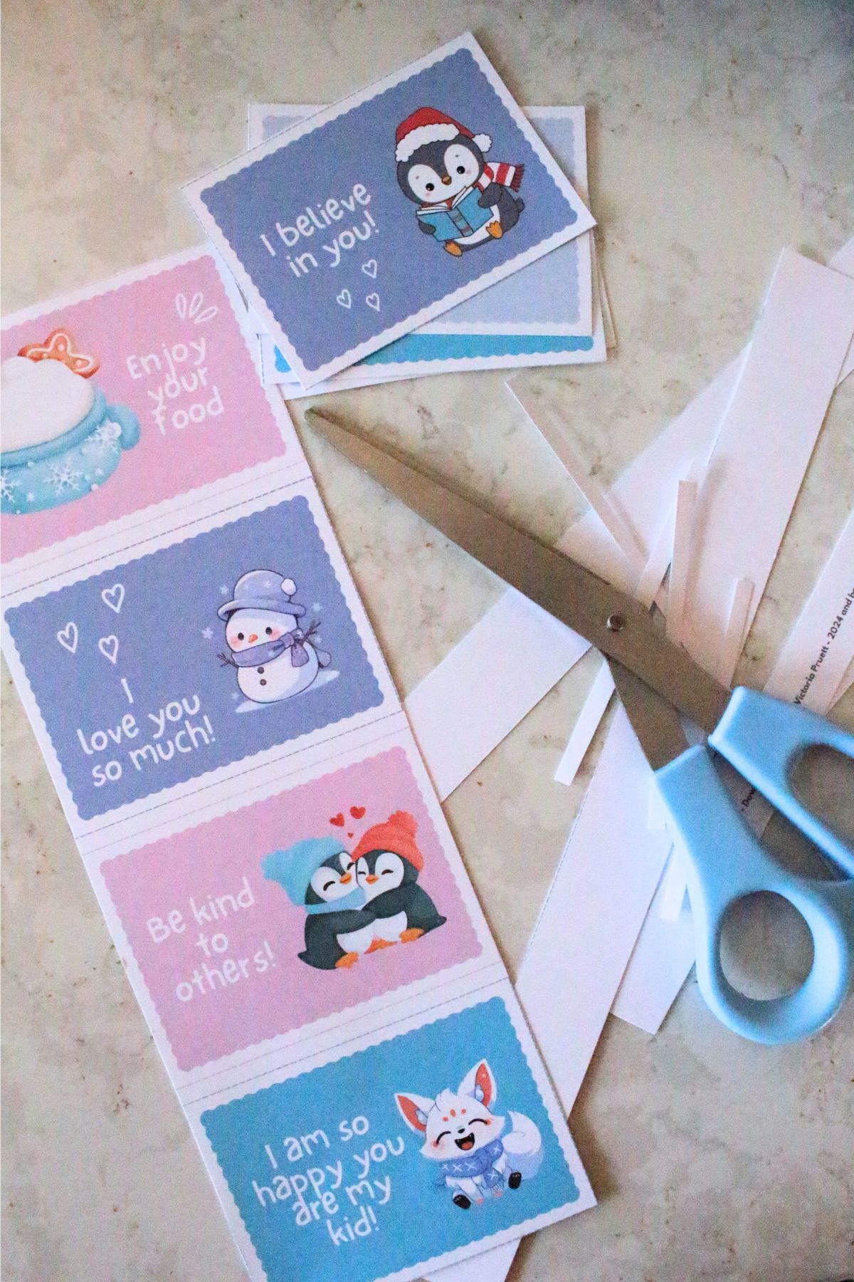 The printable winter lunch box notes being cut out with the scissors and scraps all around them